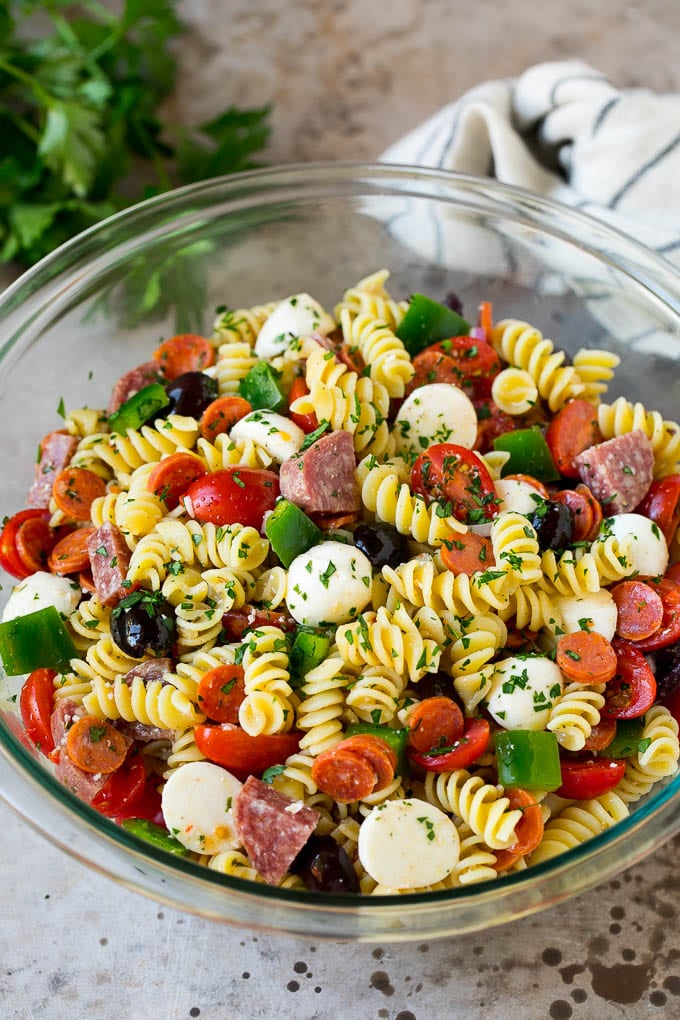 Un plato de ensalada de pasta italiana relleno de carne, queso y verduras.