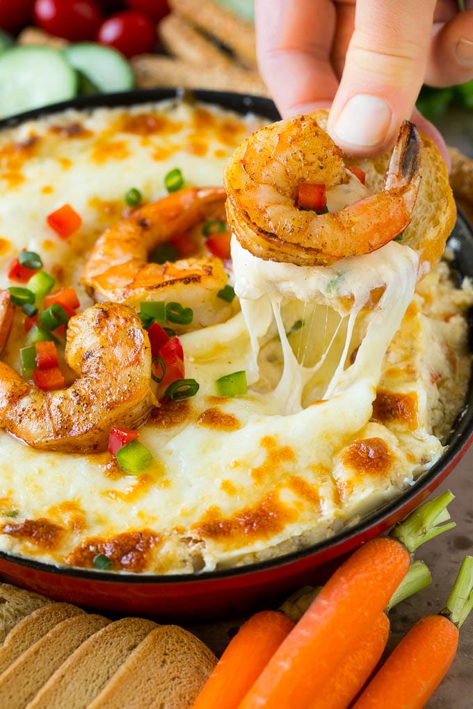 Una mano recogiendo una porción de salsa de camarones con un trozo de pan.