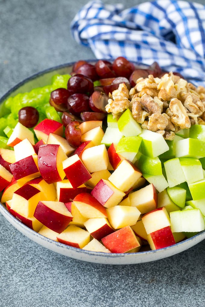 Receta de ensalada Waldorf | Ensalada de manzana | Ensalada de frutas #ensalada #frutas #manzanas #uvas #lunch #Cazuelas online#glutenfree Manzanas rojas y verdes, uvas, nueces y apio en un tazón para servir.
