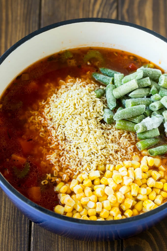 Una olla de sopa con fideos de letras, maíz congelado y judías verdes congeladas.