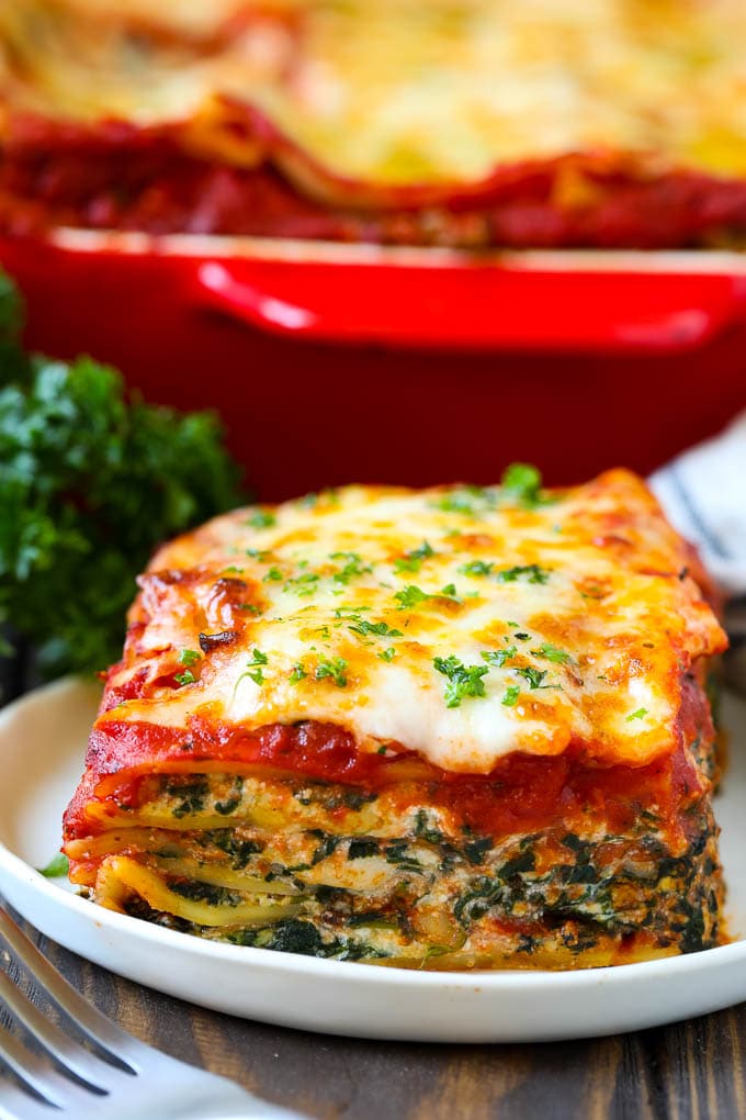Receta de lasaña de espinacas | Lasaña vegetariana #lasaña #espinacas #queso #pasta #comida italiana # cena #dinneratthezoo Un trozo de lasaña de espinacas en un plato, adornado con perejil picado.