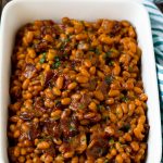 Frijoles al horno con tocino en un plato para servir aderezado con perejil.
