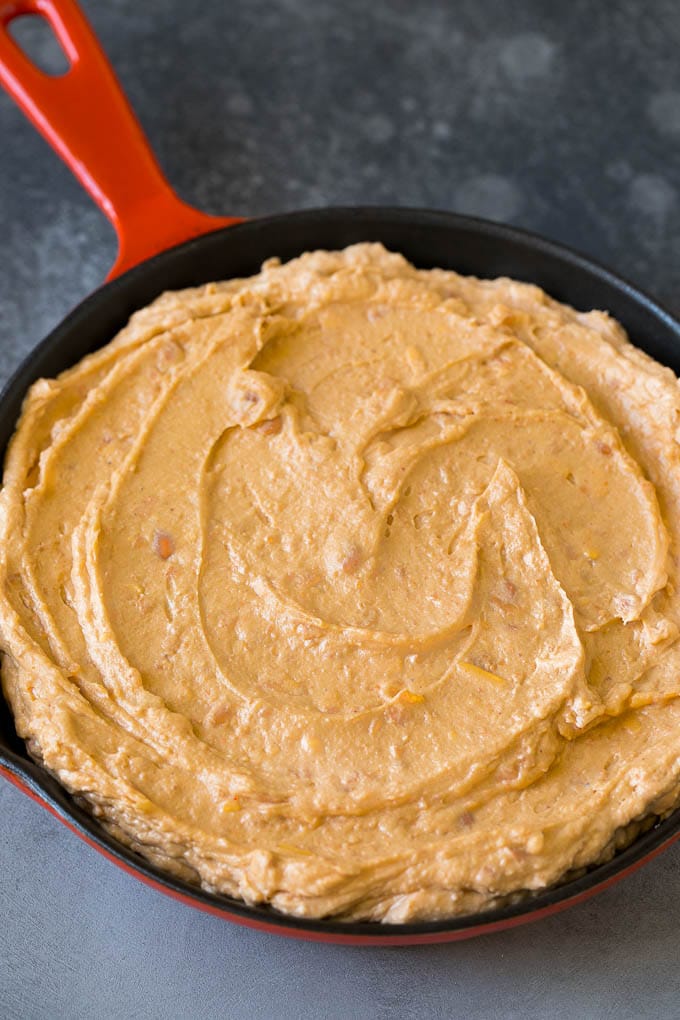 Frijoles fritos mezclados con queso crema, crema agria y condimentos en una sartén.