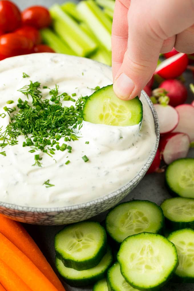 Una mano tomando un chapuzón vegetariano con una rodaja de pepino.