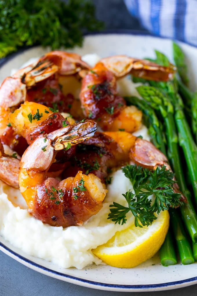 Camarones envueltos en tocino servidos sobre puré de papas con judías verdes.
