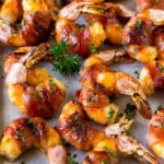 Camarones envueltos en tocino en un glaseado dulce y salado, aderezado con perejil.