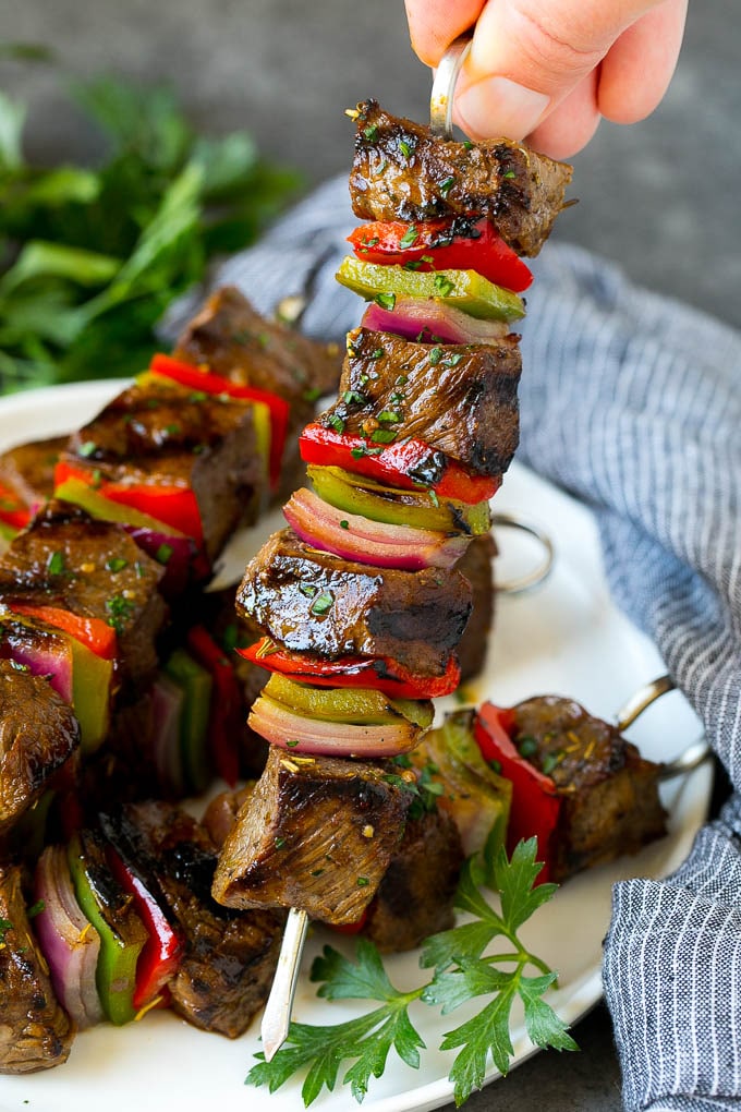 Mano sujetando una brocheta de ternera con pimientos y cebollas.