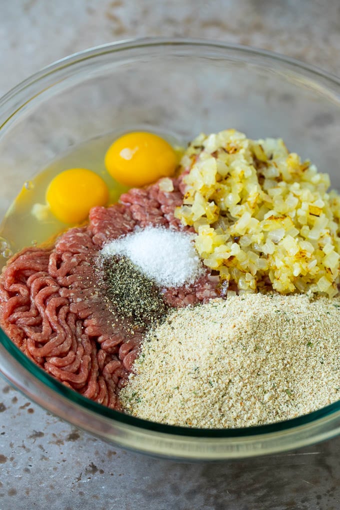 Carne molida, pan rallado, huevos, condimentos y cebollas en un bol.