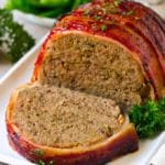 Un pastel de carne envuelto en tocino con una rebanada, en un plato para servir.