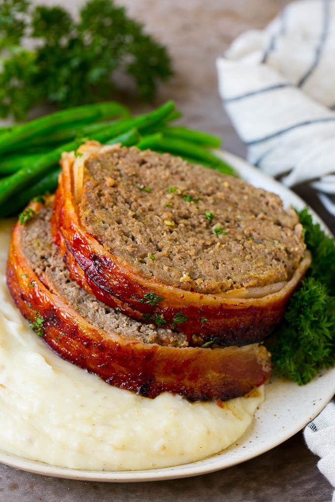 Rebanadas de pastel de carne envueltas en tocino servidas sobre puré de papas con judías verdes.