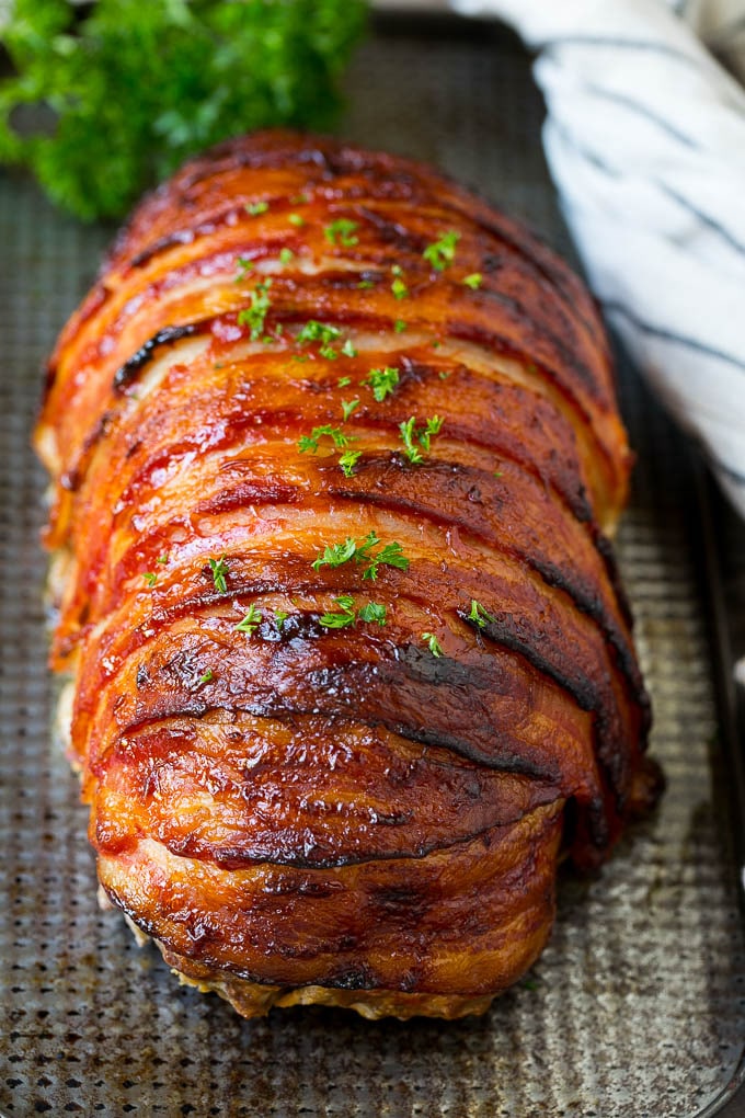 Pastel de carne envuelto en rodajas de tocino y horneado, luego adornado con perejil.