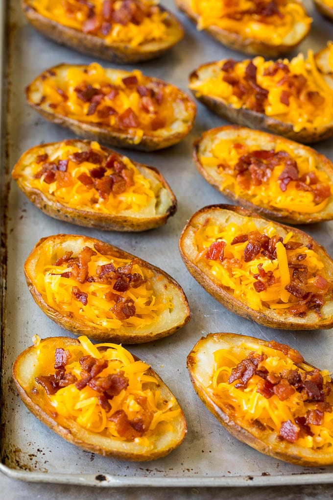 Papas al horno cortadas por la mitad cubiertas con queso rallado y tocino.