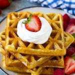 Una pila de waffles de suero de leche cubiertos con almíbar, crema batida y fruta fresca.