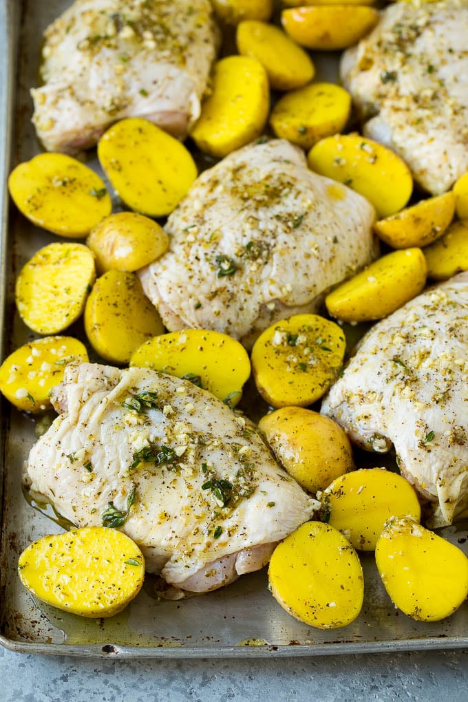 Las patas de pollo y las patatas se extienden sobre una bandeja para hornear.