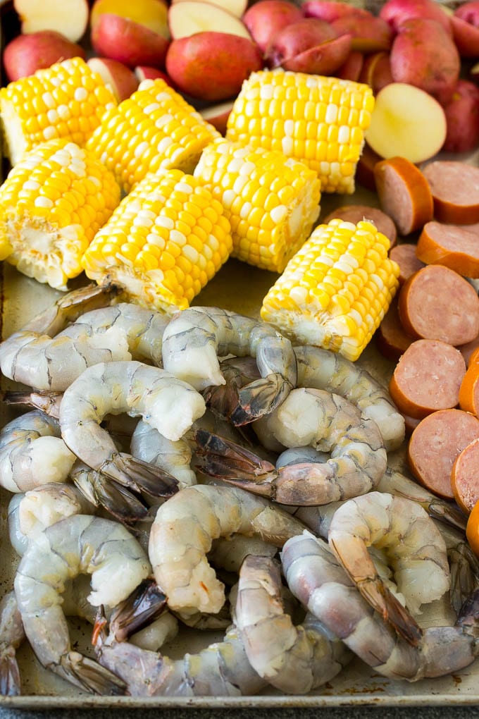 Camarones crudos, maíz, salchichas y patatas en una bandeja para hornear.