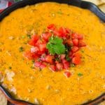 Una cacerola de salsa Rotel cubierta con tomates frescos y cilantro, servida con totopos.