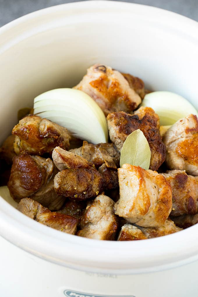 Receta de carnitas de taco de cocción lenta | Tacos de cerdo #tacos #pork # dinner #slowcooker #crockpot #dinneratthezoo Carne de cerdo, cebollas, especias y laurel en una olla de cocción lenta.