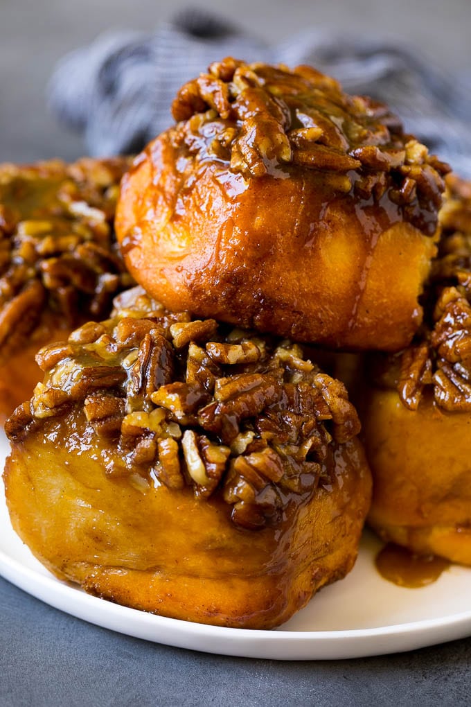 Receta de bollos pegajosos | Sándwiches dulces | Rollos de canela # desayuno # brunch # canela # nueces # Cazuelas online# pan Un plato de bocadillos pegajosos cubierto con nueces picadas.