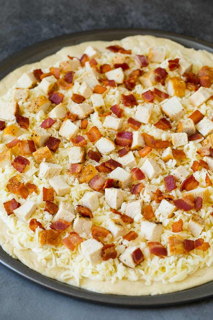 Una base de pizza cubierta con salsa alfredo, queso rallado y pollo.