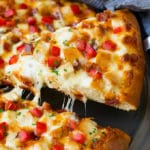 Una rebanada de pizza de pollo Alfredo con tocino fresco y tomates.