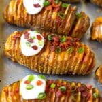 Papas Hasselback rellenas de queso derretido, luego rociadas con tocino, crema agria y cebollas verdes.