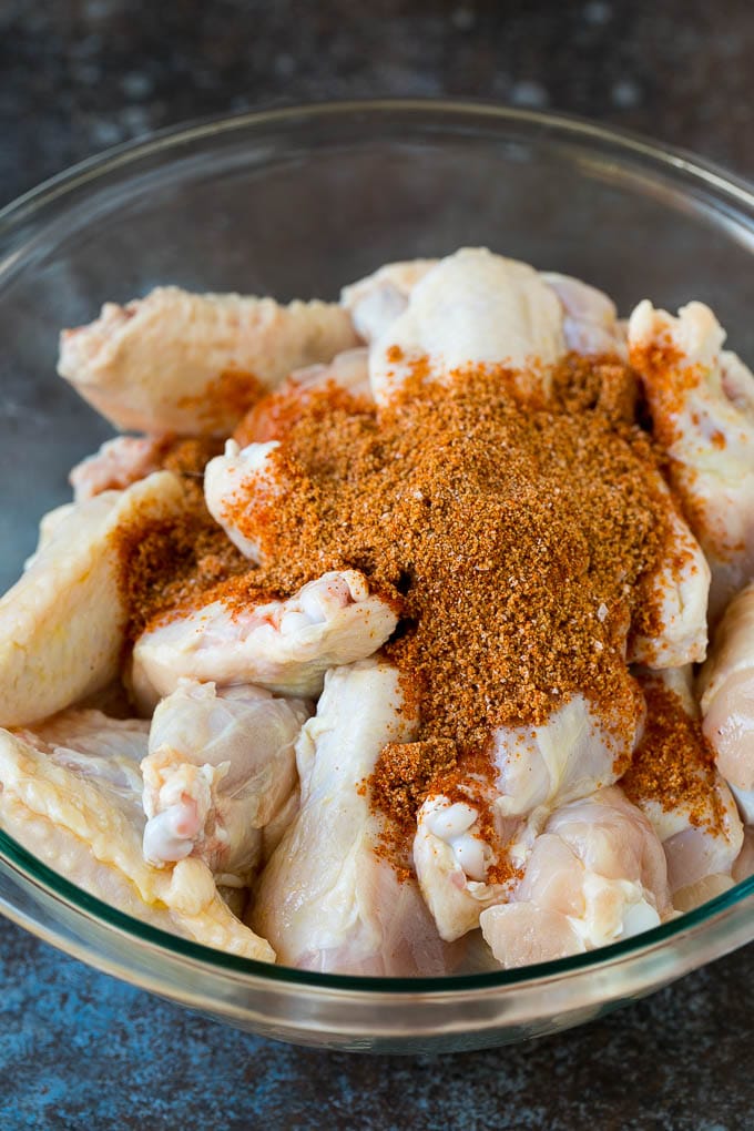 Las alitas de pollo y las especias se frotan en un tazón.