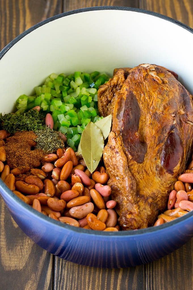 Una lata de frijoles rojos con verduras, condimentos y una pierna de jamón.