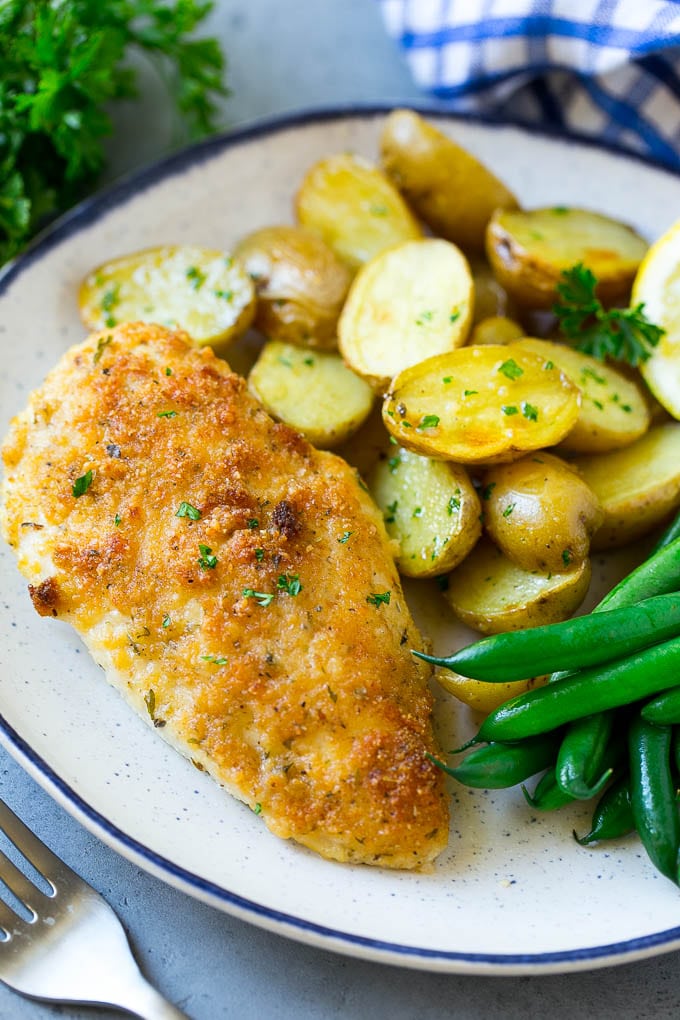 Un plato de pollo italiano, patatas asadas y judías verdes.
