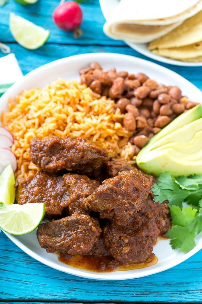 Esta receta de chile de Colorado es un platillo tradicional mexicano hecho con tierna carne de res cocinada a fuego lento en una sabrosa salsa de tomate.  ¡Es el acompañamiento perfecto para burritos, enchiladas y tacos! Un plato de carne mexicana con arroz y frijoles.