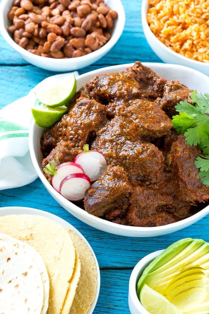 Esta receta de chile de Colorado es un platillo tradicional mexicano hecho con tierna carne de res cocinada a fuego lento en una sabrosa salsa de tomate.  ¡Es el acompañamiento perfecto para burritos, enchiladas y tacos! Estofado de carne mexicana servido con cuencos de arroz y frijoles.