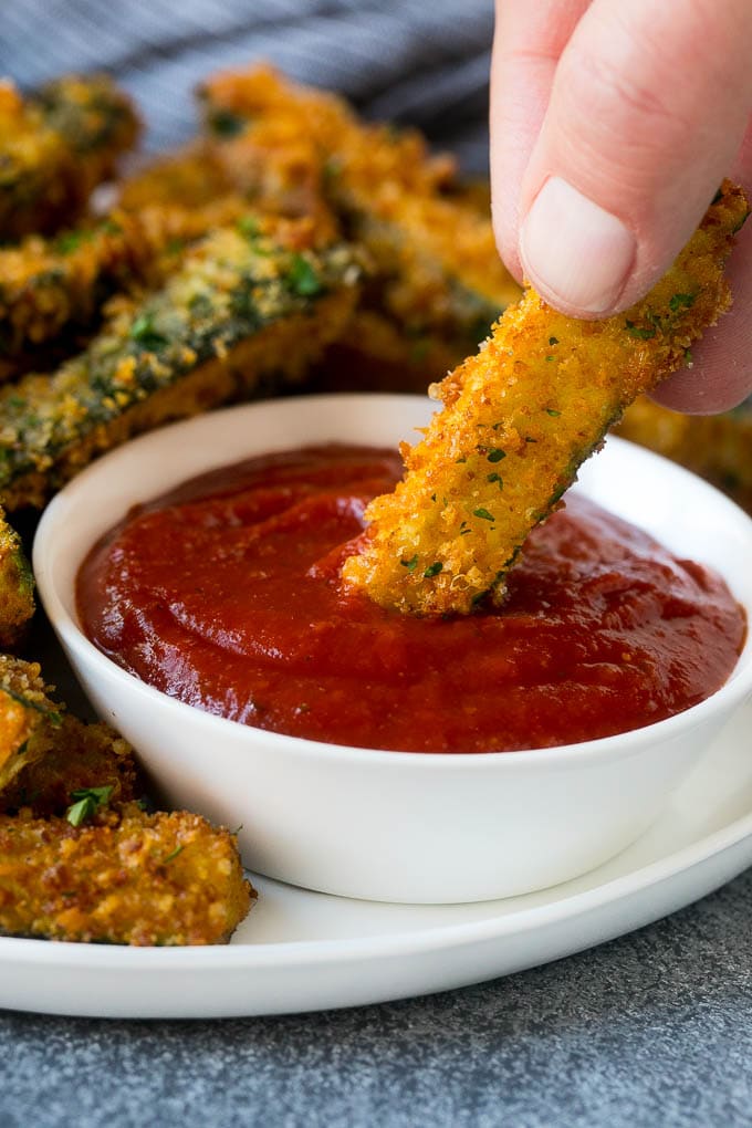 Receta de calabacín frito |  Patatas fritas de calabacín |  Receta de calabacín #aperitivo #zucchine #snack #dinneratthezoo Mojando a mano un trozo de calabacín frito en salsa marinara.