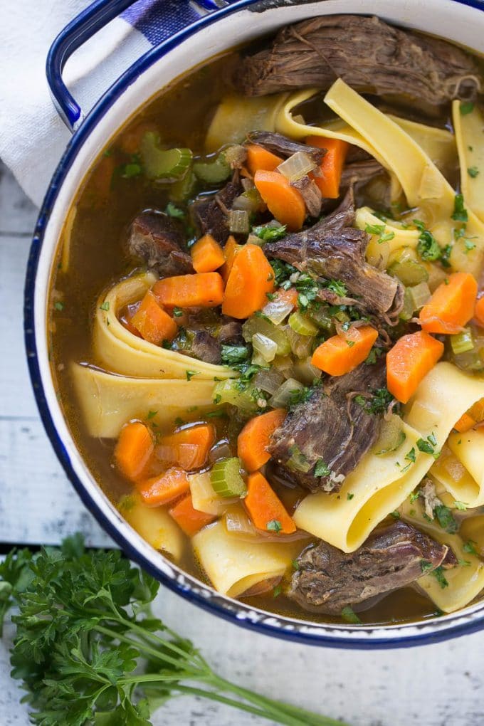 Una olla llena de sopa de ternera con fideos de huevo, zanahorias, apio y perejil.