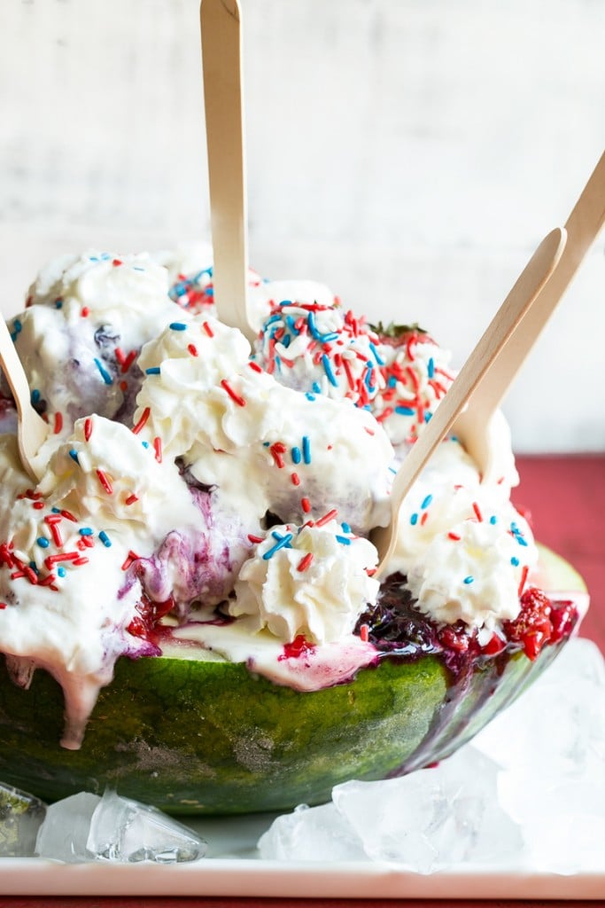 Esta receta de helado de arándano blanco es una sandía cargada con tres tipos de helado, salsas caseras de fresa y arándano, una cobertura de malvavisco, y todo termina con crema batida, chispas y chispas de fresa cubiertas de chocolate.  ¡Es el espectáculo perfecto del 4 de julio!