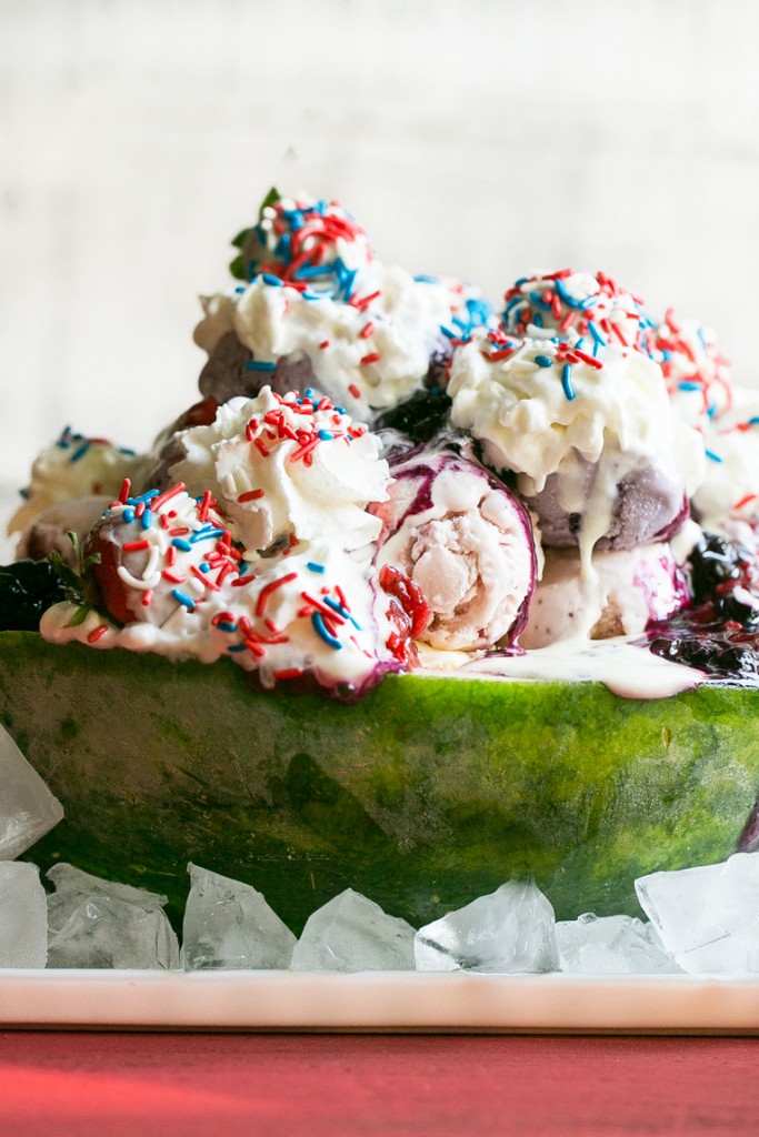 Esta receta de helado de arándano blanco es una sandía cargada con tres tipos de helado, salsas caseras de fresa y arándano, una cobertura de malvavisco, y todo termina con crema batida, chispas y chispas de fresa cubiertas de chocolate.  ¡Es el espectáculo perfecto del 4 de julio!