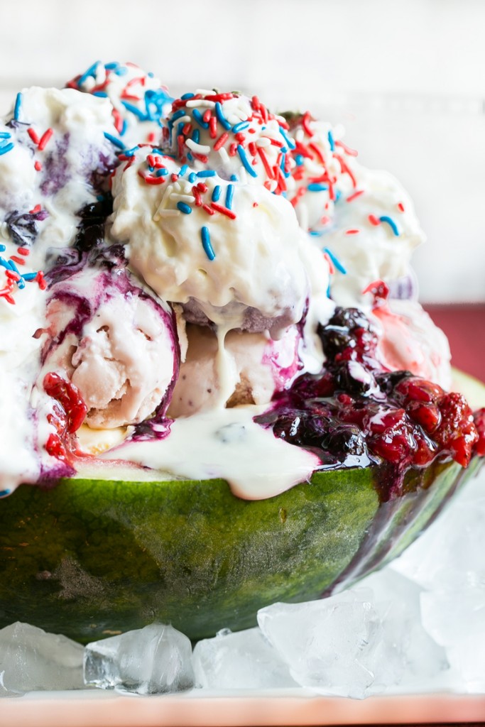Esta receta de helado de arándano blanco es una sandía cargada con tres tipos de helado, salsas caseras de fresa y arándano, una cobertura de malvavisco, y todo termina con crema batida, chispas y chispas de fresa cubiertas de chocolate.  ¡Es el espectáculo perfecto del 4 de julio!