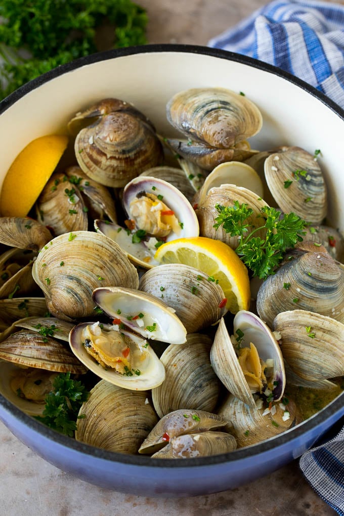 Esta receta de almejas al vapor está hecha con mariscos frescos cocidos con ajo, mantequilla, hierbas y limón. Almejas al vapor en una cacerola con rodajas de limón y perejil.