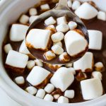 Un cucharón lleno de chocolate caliente de olla de cocción lenta cubierto con malvaviscos.
