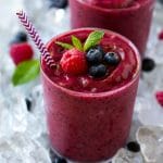 Un vaso de batido de frutas congeladas sobre hielo picado, adornado con bayas y menta.