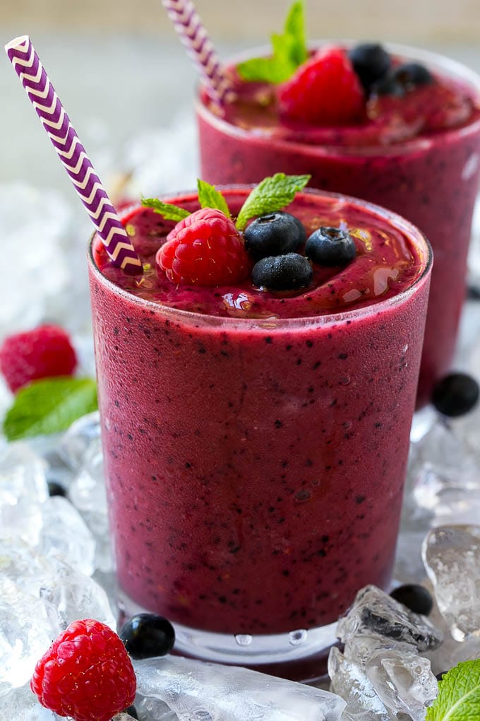 Un vaso de batido de frutas congeladas con una pajita, adornado con frambuesas, arándanos y menta.