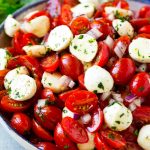 Ensalada de tomates cherry con tomates cherry cortados a la mitad, bolas de mozzarella y cebolla morada, todo aderezado con hierbas y vinagreta.