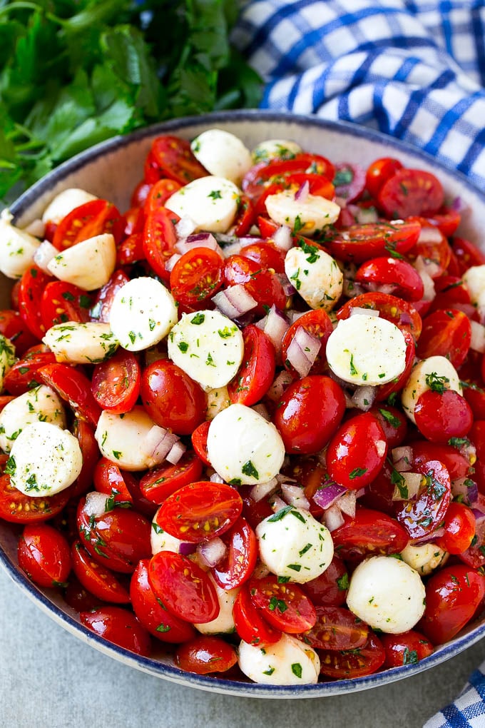 Un plato de ensalada de tomate y mozzarella con tomates cherry, hierbas y cebolla morada.