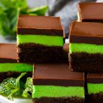Brownies de menta en capas con glaseado en un plato para servir, aderezado con menta fresca.
