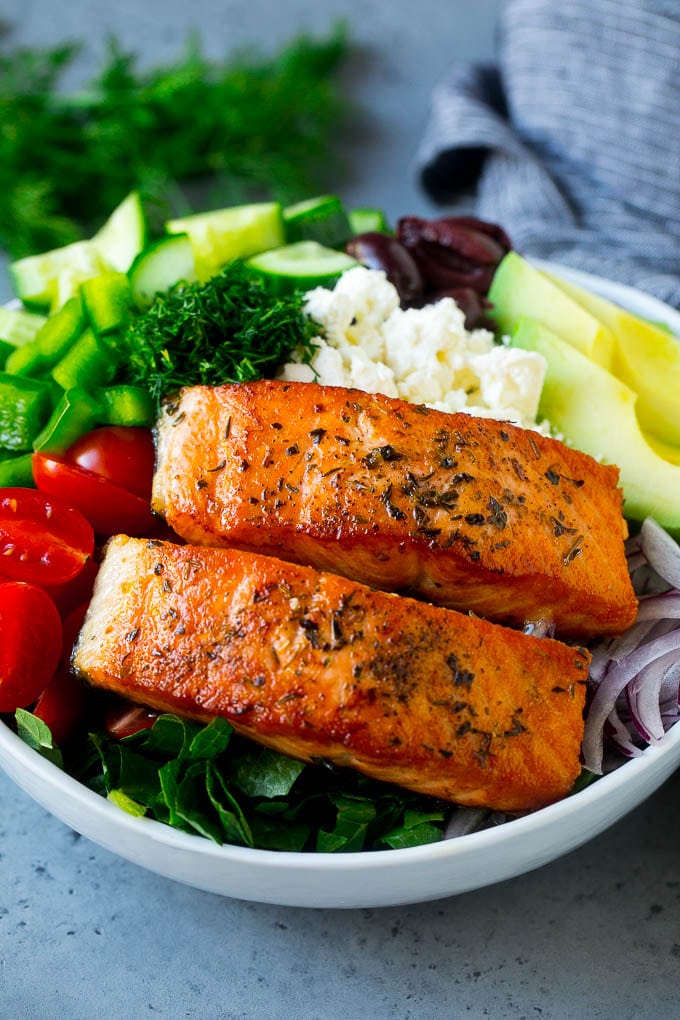 Filetes de salmón sobre lechuga con tomate, queso feta, aguacate, aceitunas, pepinos y hierbas.