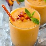 Batido de melocotón en un vaso transparente sobre una cama de hielo picado, cubierto con melocotones cortados en cubitos y menta.