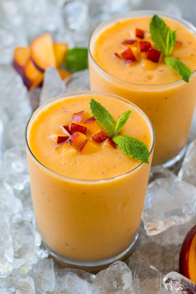 Batido de melocotón en un vaso adornado con melocotones frescos y menta.