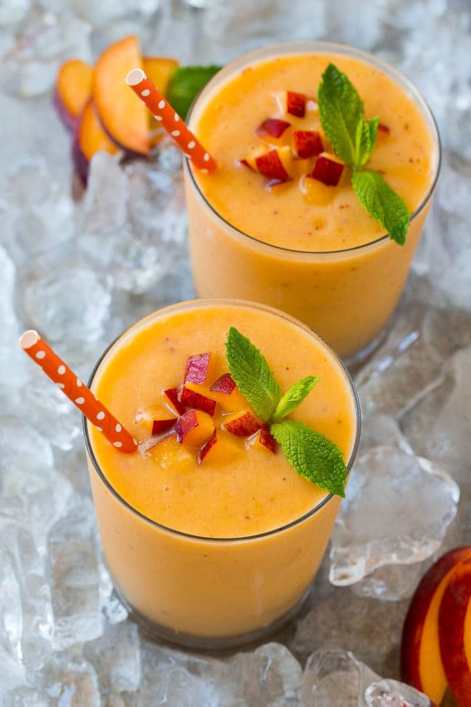 Dos vasos de batido de melocotón con hielo, aderezado con melocotones frescos.