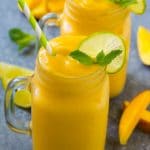 Batido de mango en una taza adornado con una rodaja de limón y una ramita de menta.