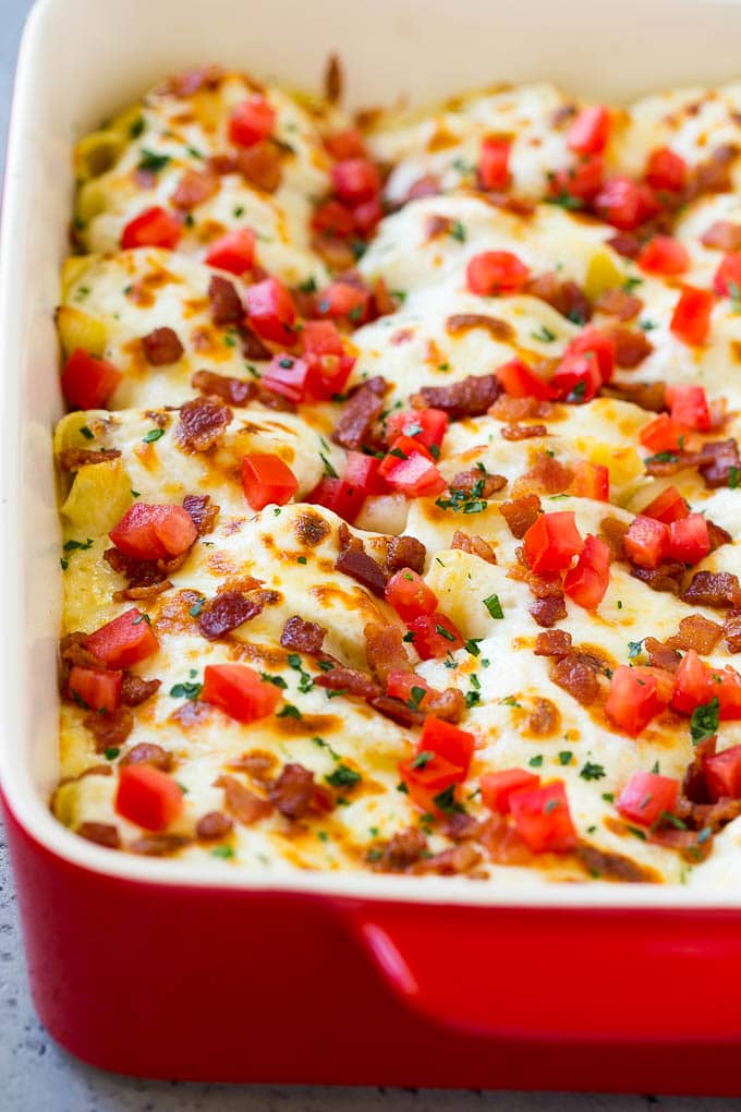 Una sartén de conchas de pollo Alfredo rellenas con queso derretido.