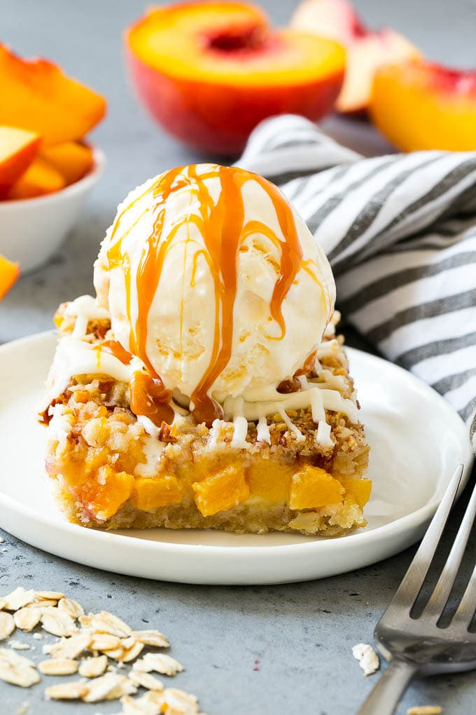 Una barra de crumble de melocotón cubierta con una bola de helado de vainilla y salsa de caramelo salado.