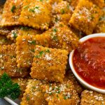 Un plato de ravioles fritos aderezado con parmesano y perejil y servido con una guarnición de salsa marinara.